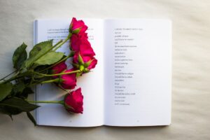 A person flipping through a poetry book next to a steaming mug and a notebook on a wooden table.