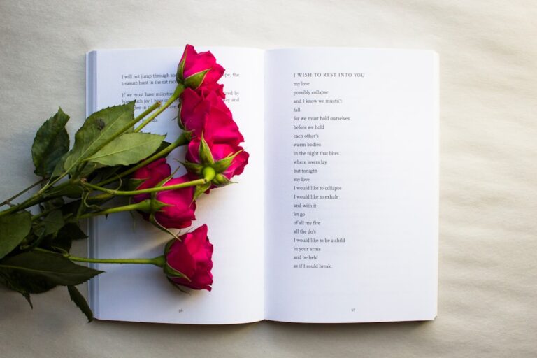 A person flipping through a poetry book next to a steaming mug and a notebook on a wooden table.