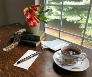 A person revises a handwritten poem at a table beside a window with notebooks and a pencil.