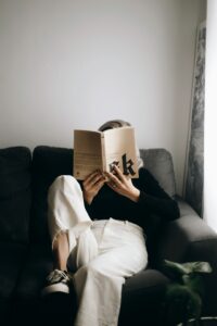 A person reads an open poetry book aloud at a table beside a window.